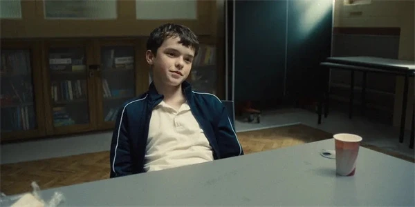 A boy sits at a table with a cup, appearing calm in "Adolescence".