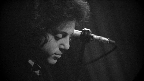 Billy Joel near a microphone in "Billy Joel: And So It Goes".
